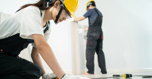 Frau mit gelbem Helm und Schutzbrille bei der Arbeit am Fußboden