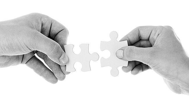zwei Hände halten Puzzleteile in der Mitte zusammen