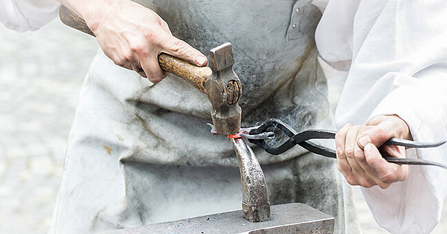 Handwerker bearbeitet mit Hammer und Zange ein Metallstück